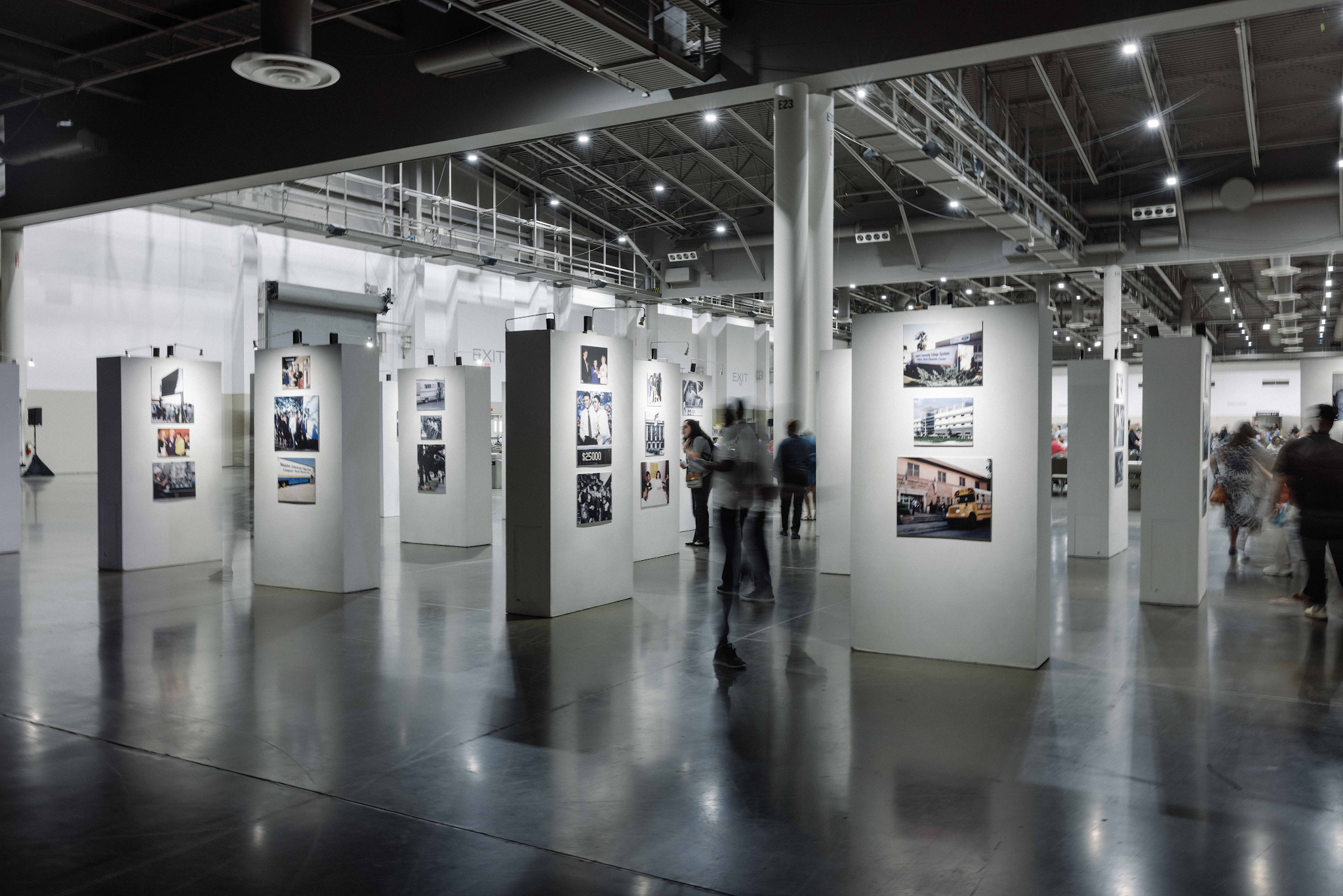 An exhibition layout with multiple white gallery walls and photographs in an industrial museum space.